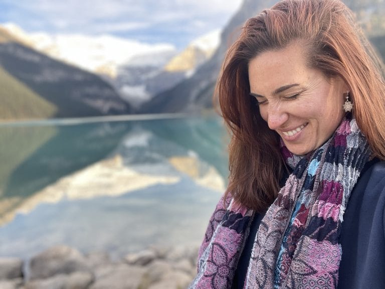 Heidi, the author, with a colorful scarf posing in front of the colorful Lake Louise