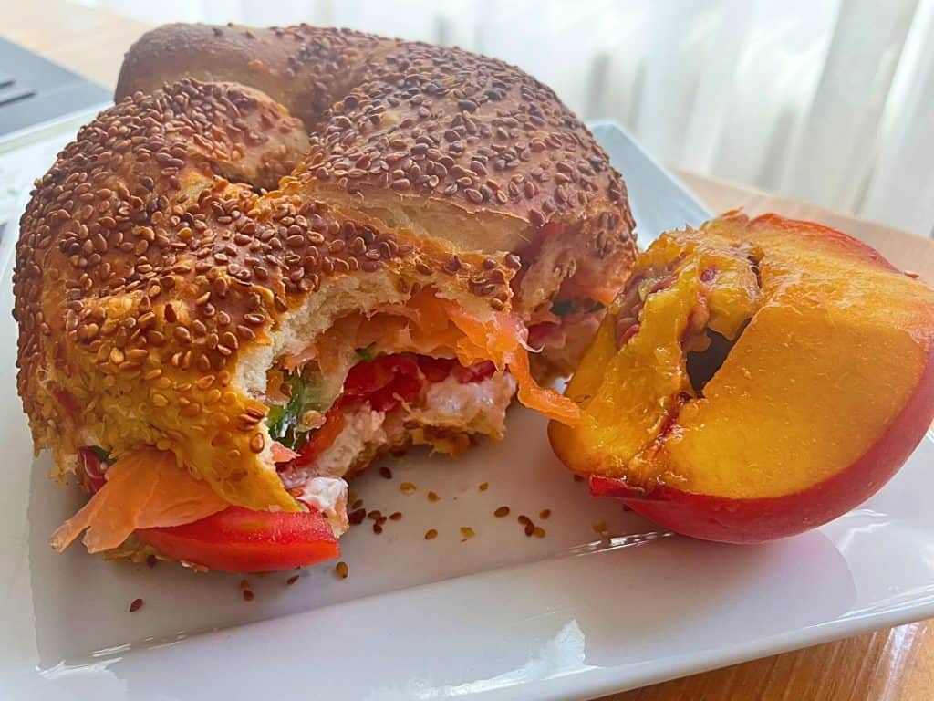 Homemade healthy sandwich on a plate with a half-eaten peach on the side