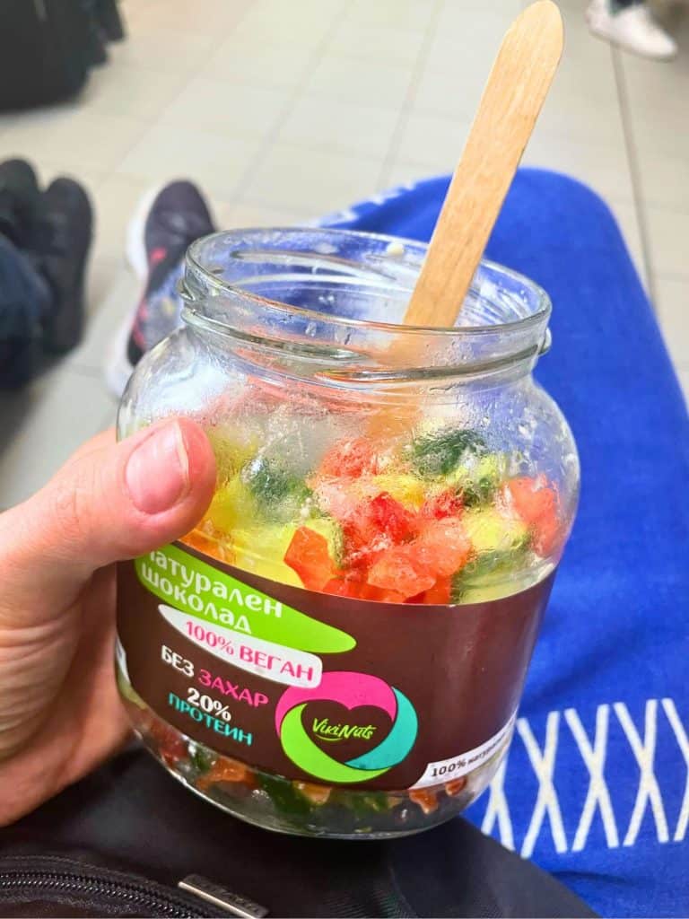 Reused jar being held in a hand showing a salad inside with a reuseable bamboo spoon sticking out at the top