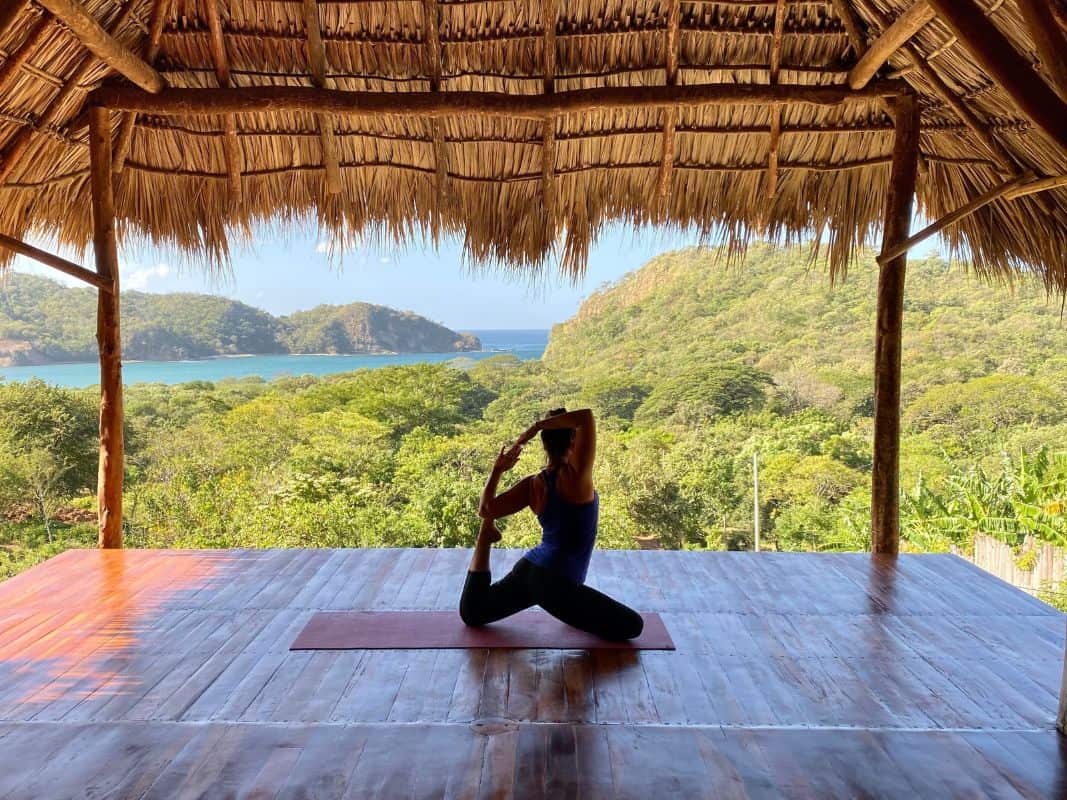 Heidi, the author, doing a seated mermaid pose on a yoga mat looking out to green jungle and lake
