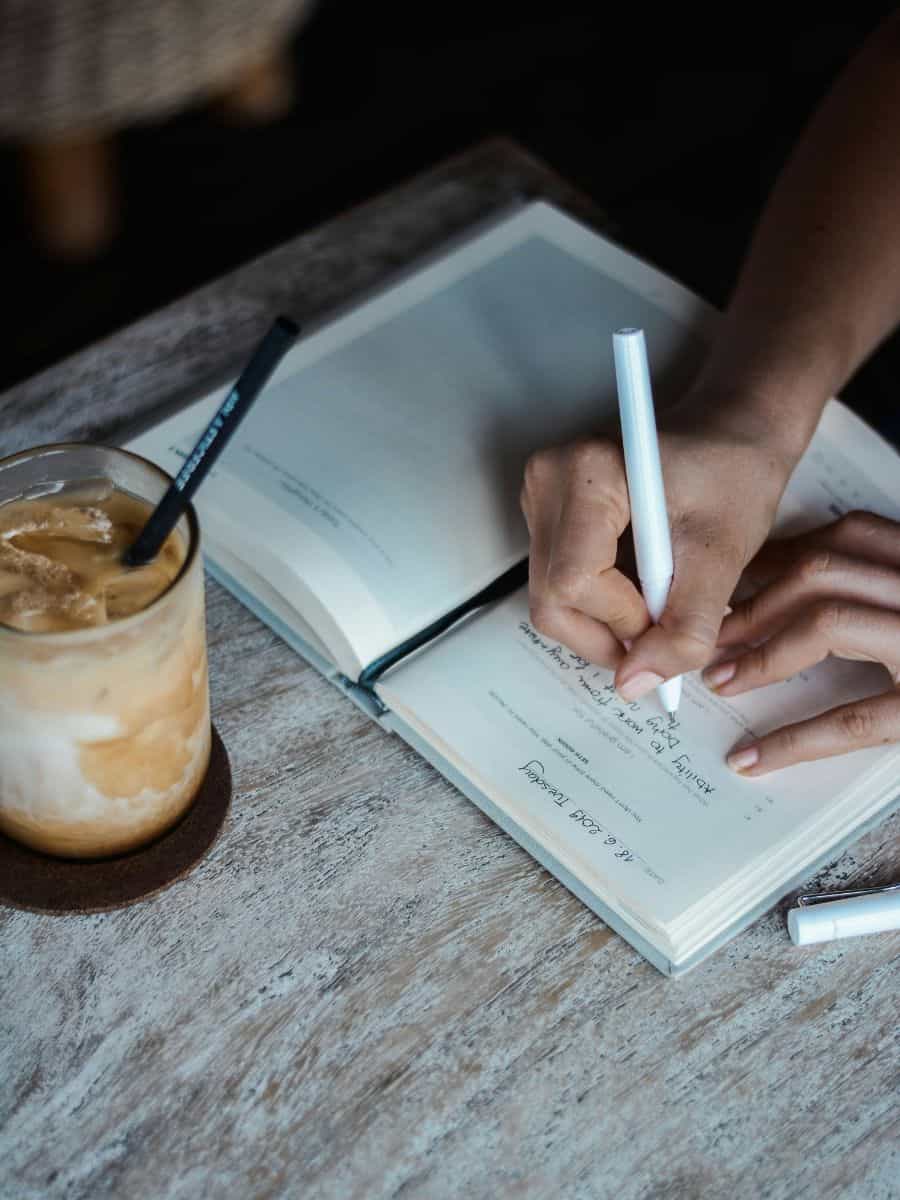 Someone writing in a journal with an iced coffee