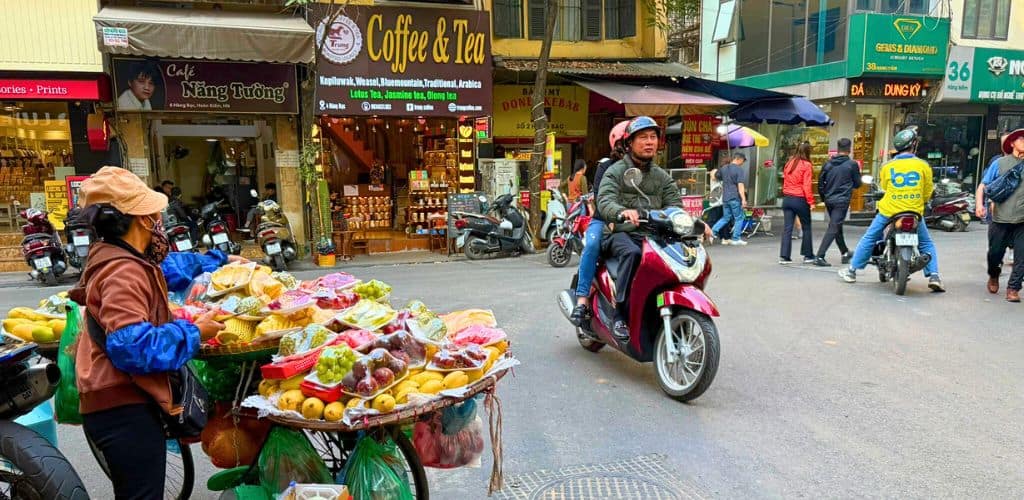 Busy Hanoi street with someone on a motorbike and another selling fruit