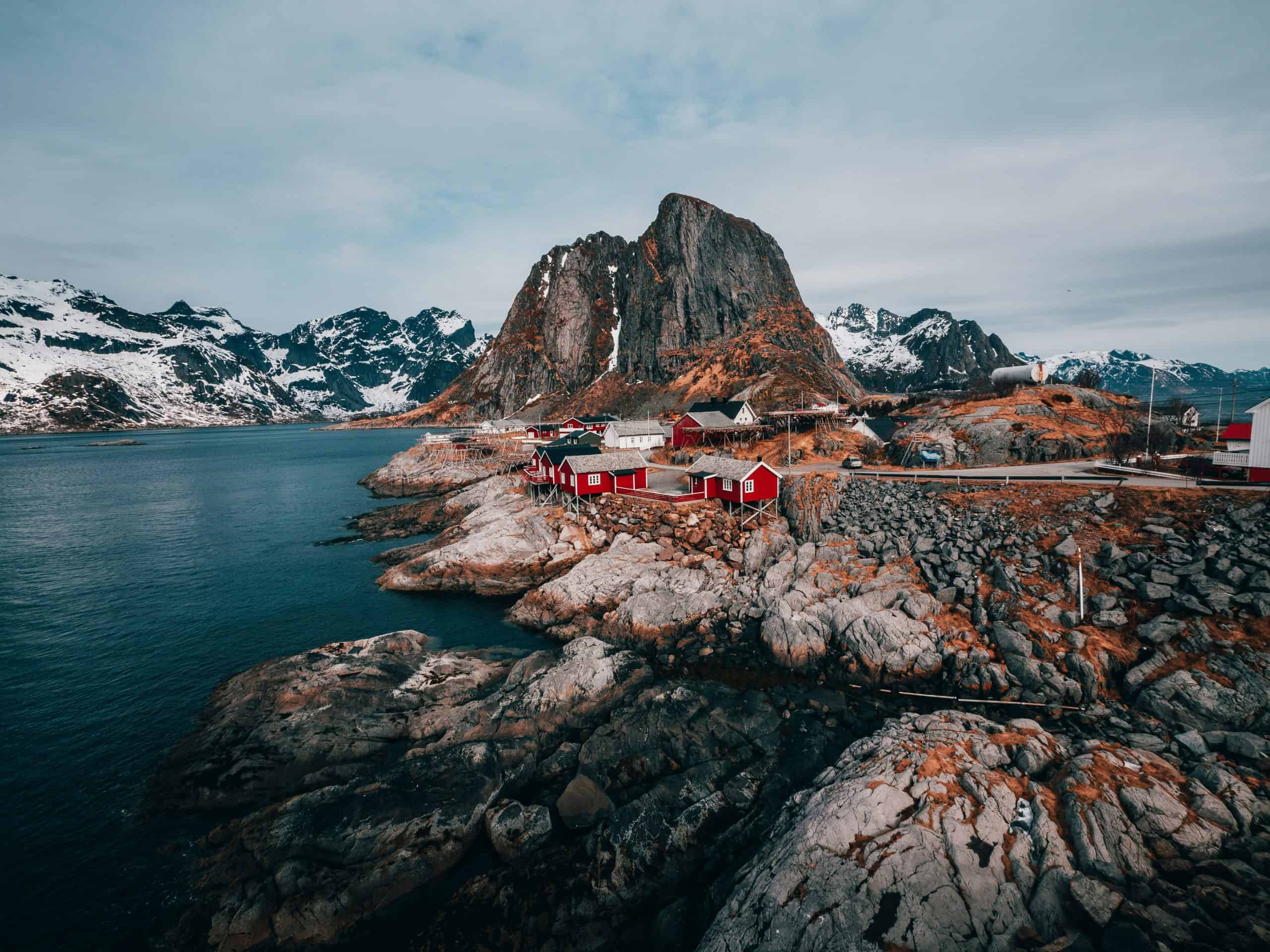 Water and cliffs.  There are snowy cliffs in the distance.  There are some small red and white houses in the foreground and a mountain in the middle.