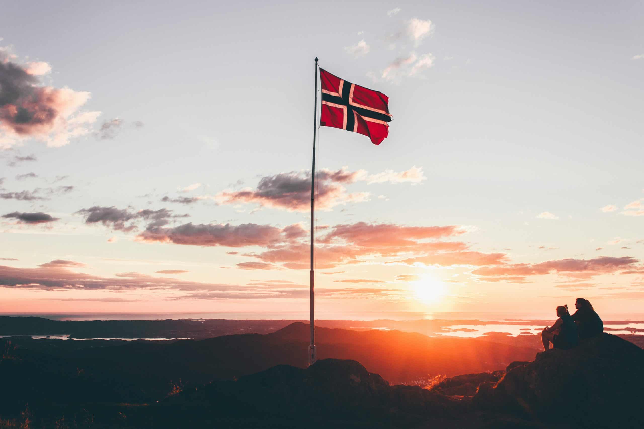 Sunset scenery with two hikers sitting on some rocks with a Norway flag