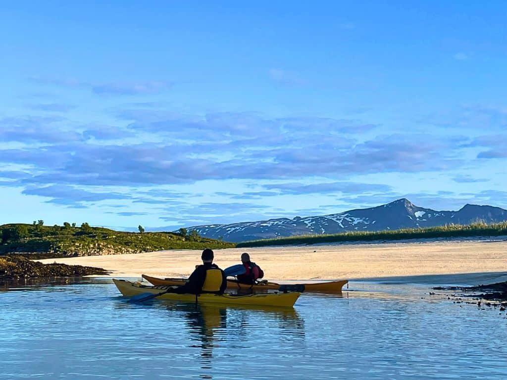 Two people out on yellow kayaks.  The water looks golden in the distance and there are snowy mountains in the backdrop.