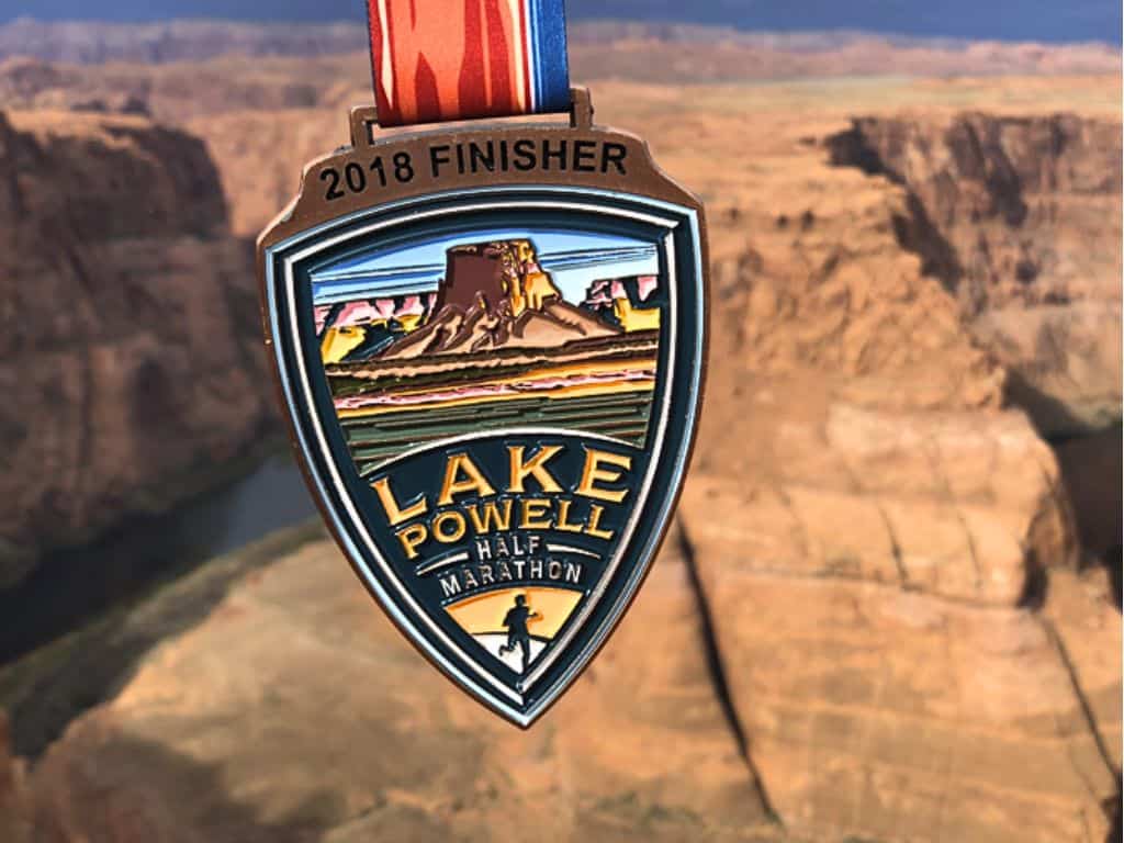 Up close view of the 2018 finisher medal for the Lake Powell half marathon.  In the background there's the red orange canyons.