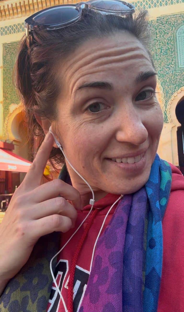 Traveler standing in front of the blue gate in Fes, Morocco pointing to her wired headphones
