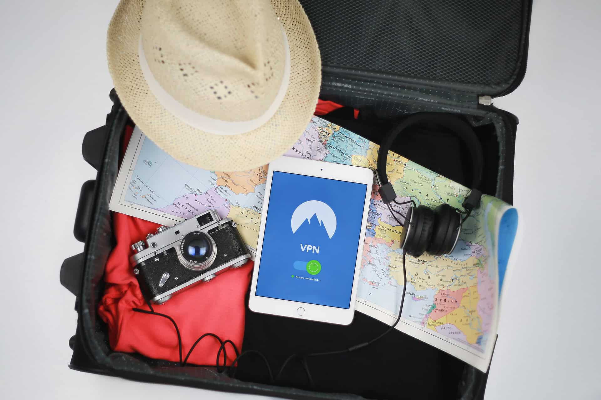 Open suitcase with various packed items like a map, headphones, tablet, camera, hat, and clothes