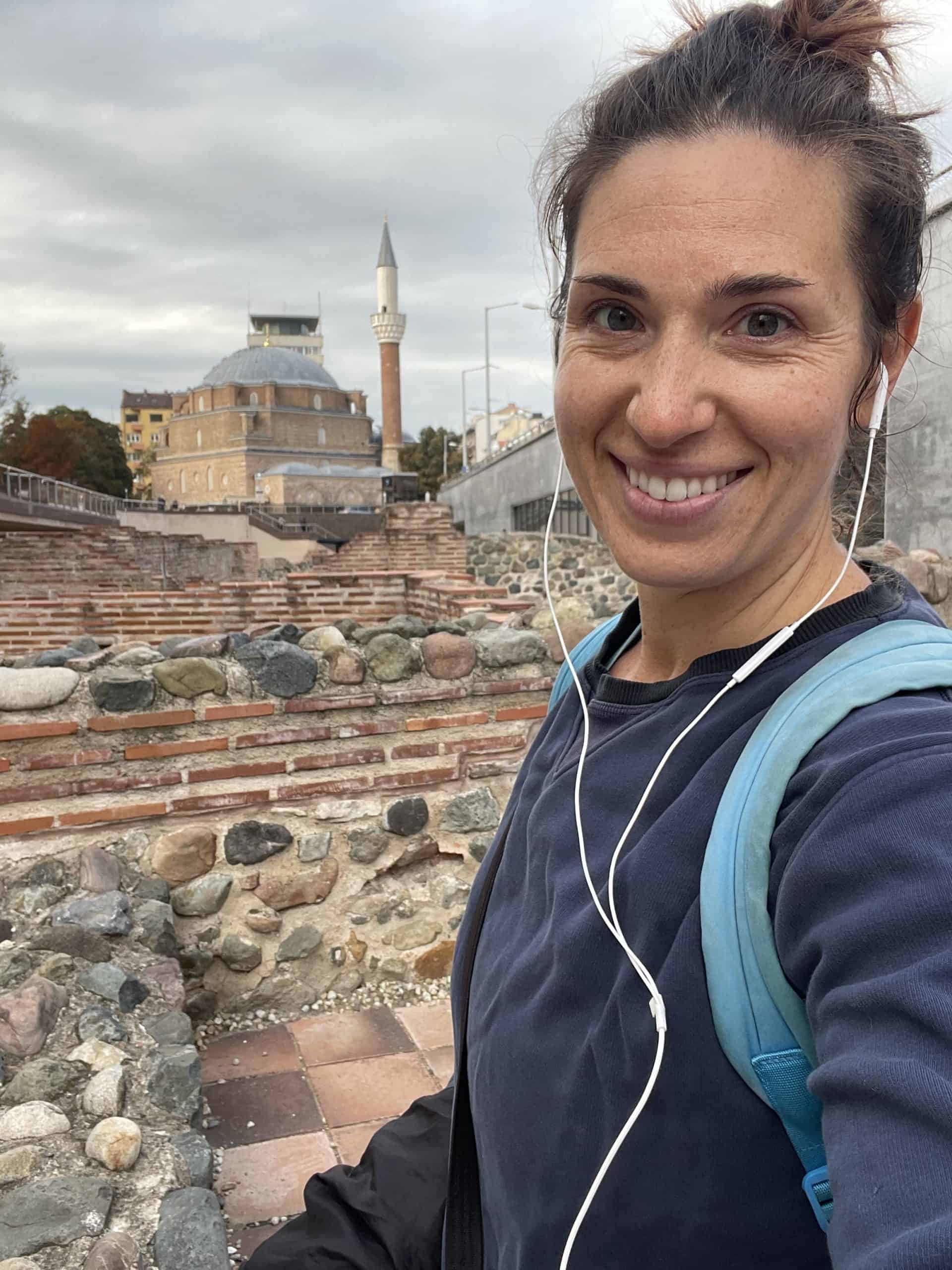 Heidi smiling in Sofia ruins while wearing headphones and a backpack
